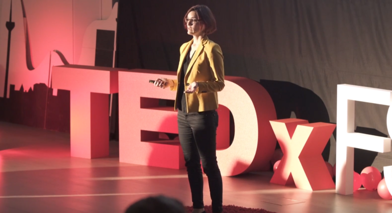 Katharina Brinck steht auf der Bühne vor dem roten TEDx Logo und hält einen Vortrag über die Bedeutung von Nachhaltigkeit bei TEDxTalk