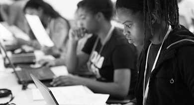 Schwarzweiß Aufnahme von jungen Menschen in schwarzer Kleidung vor ihren Laptops. Junge Menschen symbolisieren hier Innovation und Kommunikation.